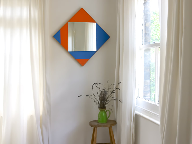 Hand made square wall mirror with orange and blue panels in a room by a window